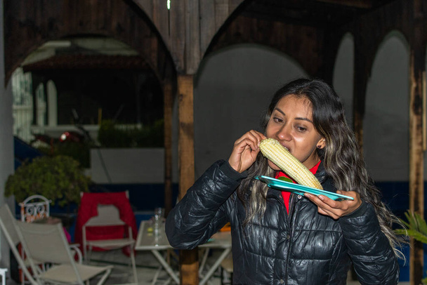 Nainen hauskaa yllään musta takki ja syö maissia - Valokuva, kuva