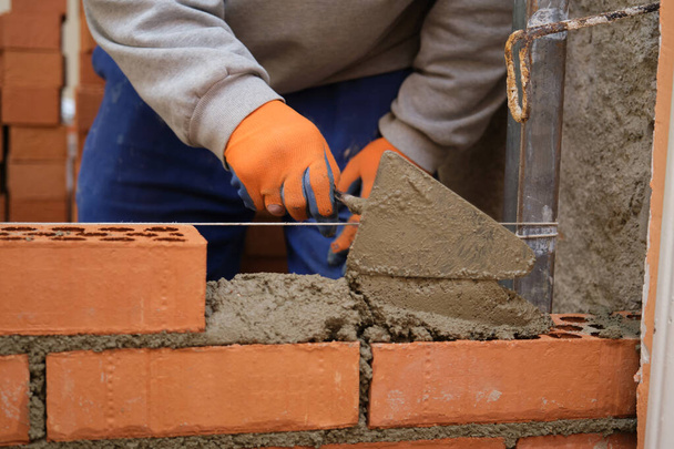 Stavební dělník dává beton na cihlovou zeď. Zednické práce. Mason kladení cihel. - Fotografie, Obrázek