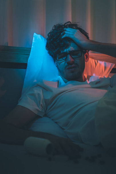 Przygnębiony bezsenność biały człowiek trzymając głowę na łóżku późno w nocy z Black Medical pigułki na stres i koncepcja samobójstwa. - Zdjęcie, obraz