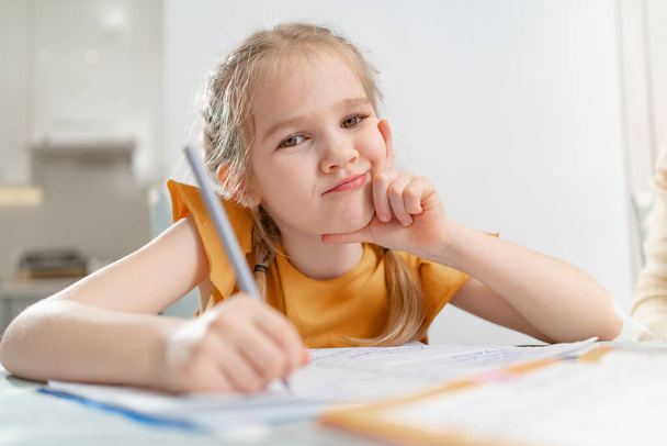 Düşünceli küçük bir okul kızı ödevini yapıyor..  - Fotoğraf, Görsel
