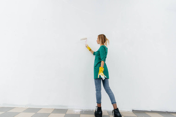 A young girl paints a white wall with a roller. Repair of the interior. - Foto, Imagem