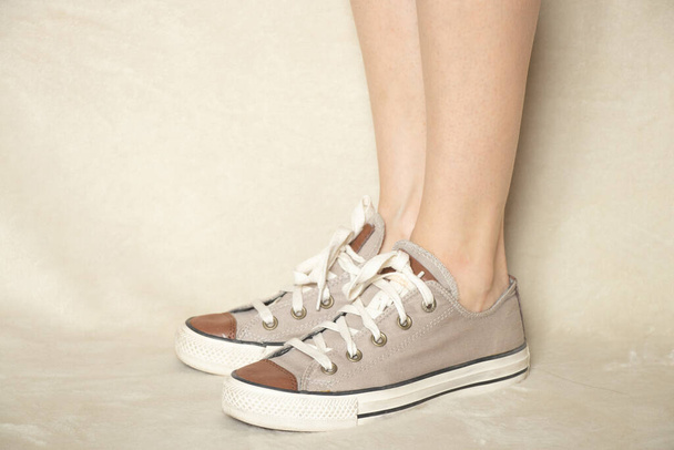 vrouwelijke benen in textiel bruine sneakers op een witte achtergrond close-up - Foto, afbeelding