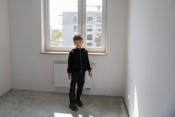 Ευτυχισμένο νεαρό αγόρι στο νέο άδειο δωμάτιό του στο νέο διαμέρισμα - Φωτογραφία, εικόνα