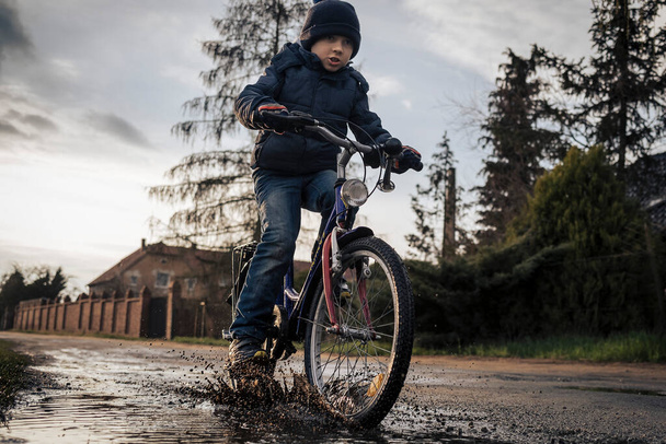 Fiatal fiú biciklizik a pocsolyánál a földúton. - Fotó, kép