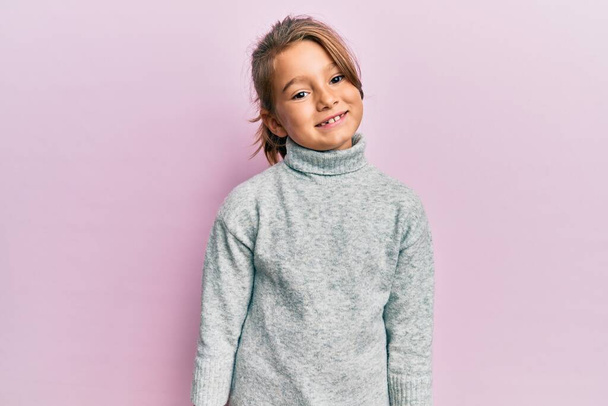 幸せとクールな笑顔でカジュアルなタートルネックセーターを身に着けている小さな美しい女の子。運のいい人.  - 写真・画像