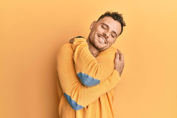 Jeune homme hispanique portant des vêtements décontractés s'embrassant heureux et positif, souriant confiant. amour de soi et soins de soi  - Photo, image