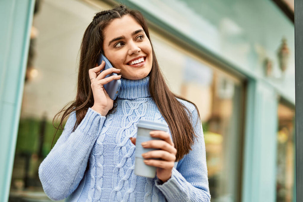 Jovencita hispana hablando en el smartphone y tomando café en la ciudad - Foto, Imagen