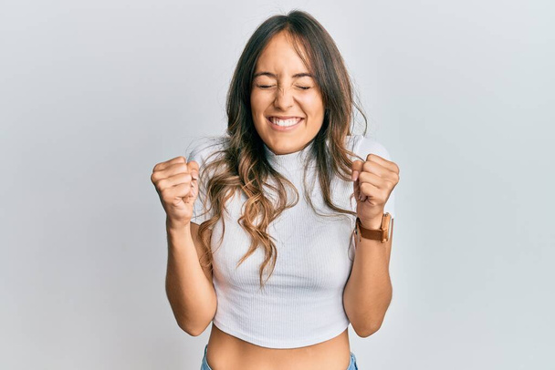 Young brunette woman wearing casual white t shirt excited for success with arms raised and eyes closed celebrating victory smiling. winner concept.  - Fotografie, Obrázek