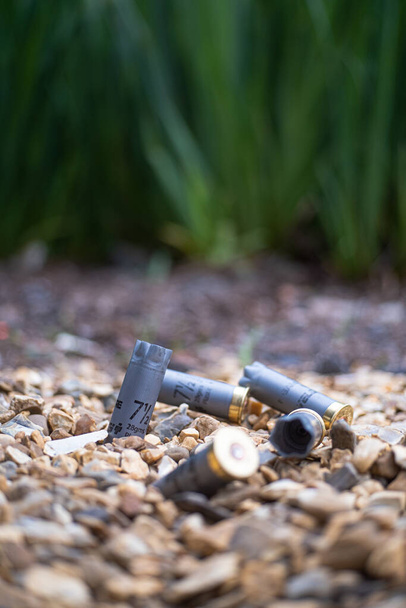 Varios cartuchos de escopeta gris gastados en el suelo en una zona de tiro público. Conceptos de peligro, acción, tiro y guerra - Foto, Imagen