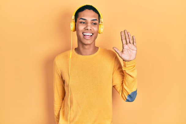 Jeune homme afro-américain écoutant de la musique à l'aide d'écouteurs montrant et pointant vers le haut avec les doigts numéro cinq tout en souriant confiant et heureux.  - Photo, image