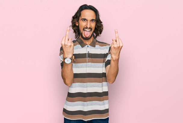 junger hispanischer Mann in lässiger Kleidung, der den Mittelfinger zeigt, wie er dich fickt, schlechte Miene, Provokation und unhöfliche Haltung zeigt. Kreischen erregt  - Foto, Bild
