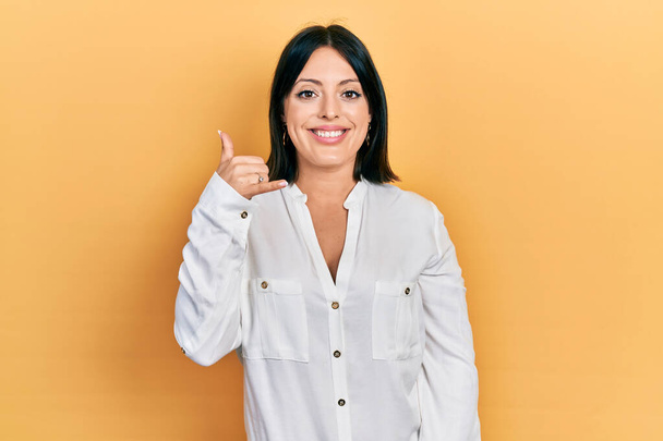 Mujer hispana joven vistiendo ropa casual sonriendo haciendo gesto telefónico con la mano y los dedos como hablando por teléfono. comunicar conceptos.  - Foto, imagen