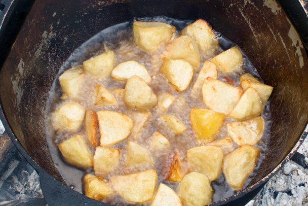 outdoor cooking. potatoes are fried in boiling oil in black cauldron over open fire. close up view - Photo, Image