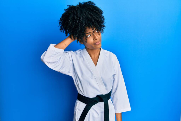 Femme afro-américaine aux cheveux afro portant kimono karaté et ceinture noire confondre et questionner sur la question. incertain avec doute, pensant la main sur la tête. concept coûteux.  - Photo, image