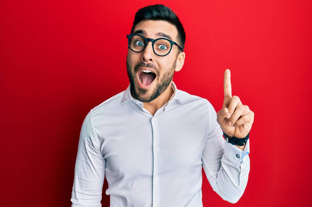 Молодий іспаномовний бізнесмен у сорочці та окулярах вказує пальцем на успішну ідею. вичерпаний і щасливий. номер один
.  - Фото, зображення
