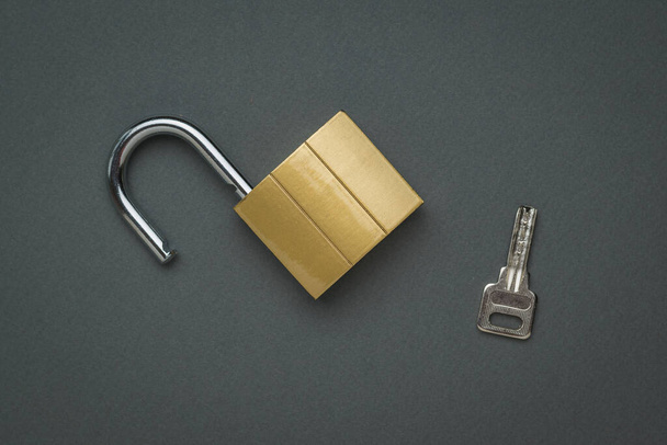 Une serrure ouverte et la clé sur un fond gris foncé. Le concept de protection et de sécurité. Pose plate. - Photo, image