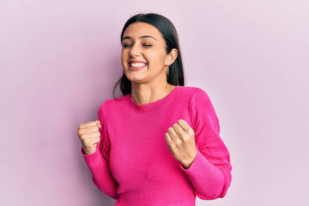 Jeune femme hispanique portant des vêtements décontractés très heureux et excité faisant geste gagnant avec les bras levés, souriant et criant pour le succès. concept de célébration.  - Photo, image