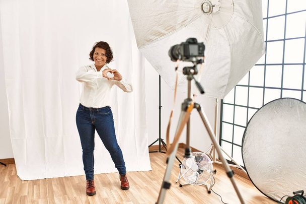 Middle age hispanic woman posing as model at photography studio smiling in love showing heart symbol and shape with hands. romantic concept.  - Fotografie, Obrázek
