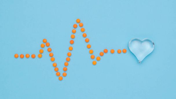 A cardiogram of pills resting on a glass heart. The concept of treatment of heart diseases. Flat lay. - Foto, Bild