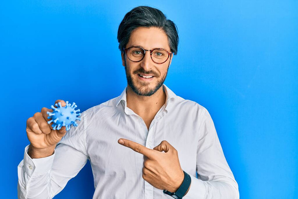 Jeune homme hispanique tenant jouet virus souriant heureux pointant avec la main et le doigt  - Photo, image