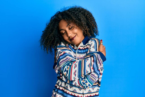 Beautiful african american woman with afro hair wearing casual clothes hugging oneself happy and positive, smiling confident. self love and self care  - Foto, Imagem