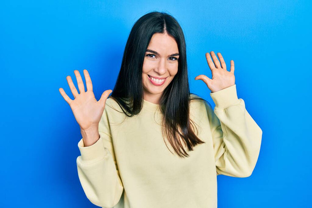Giovane donna bruna indossa felpa casual mostrando e indicando con le dita il numero dieci mentre sorride fiducioso e felice.  - Foto, immagini