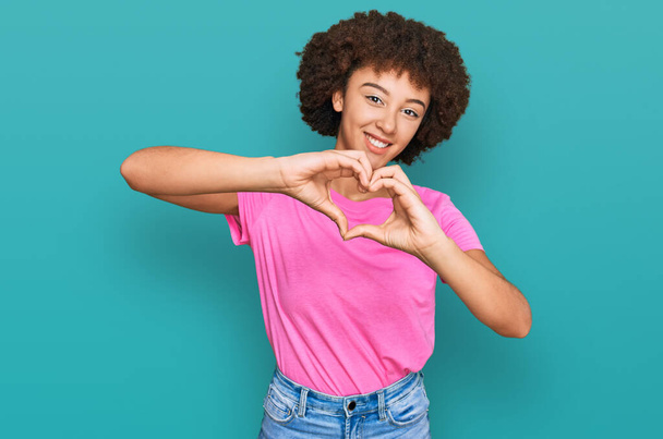 Fiatal spanyol lány alkalmi ruhát visel mosolyogva a szerelemben csinál szív szimbólum alakú kezekkel. romantikus koncepció.  - Fotó, kép