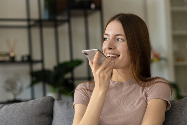 Hermosa joven linda mujer caucásica disfruta de una agradable conversación móvil en el teléfono móvil mientras se sienta en casa en el sofá - Foto, Imagen