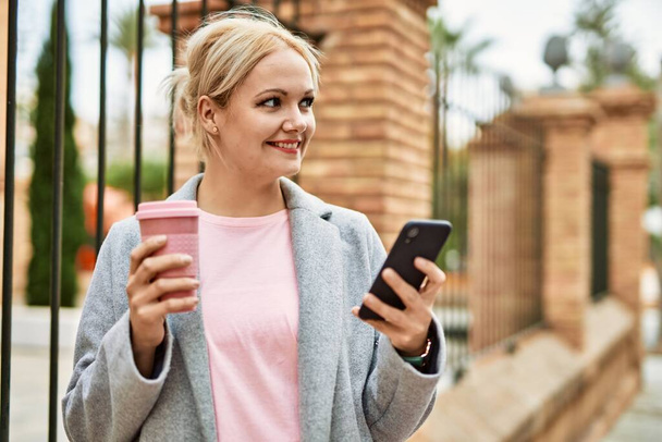 Young blonde businesswoman using smartphone drinking coffee at the city. - Foto, imagen