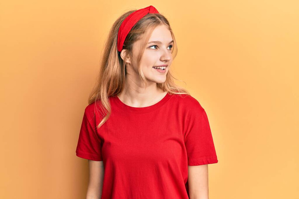 Schöne junge kaukasische Mädchen tragen lässig rotes T-Shirt mit Blick zur Seite, entspannen Profil Pose mit natürlichem Gesicht und selbstbewusstem Lächeln.  - Foto, Bild