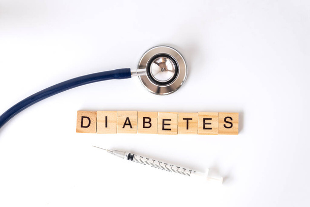 Closeup medische stethoscoop en Houten letter blok woord diabetes met insuline spuit op witte achtergrond met behulp van als diabetes, glykemie, gezondheidszorg en mensen concept. - Foto, afbeelding