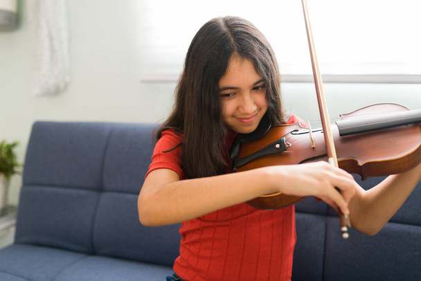 Child playing the violin. Smiling latin girl practicing her music lessons at home. Young student taking online classes to learn to play a new instrument - Foto, imagen