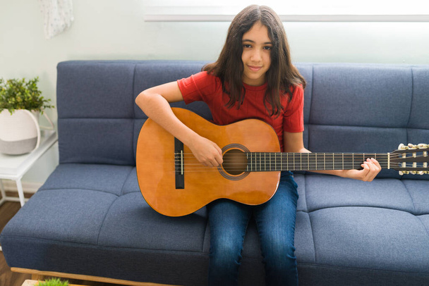 Portrait of a creative kid playing an acoustic instrument and learning the guitar chords with her home music lessons - Photo, Image