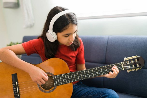A prática é perfeita. Menina bonita hispânica memorizando e praticando os acordes de guitarra em seu instrumento acústico  - Foto, Imagem