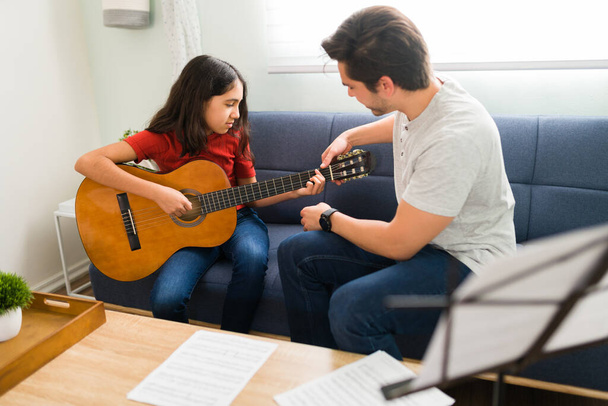 Basic guitar chords. Pretty girl learning and practicing playing a new musical instrument with a male teacher during home lessons - Фото, изображение