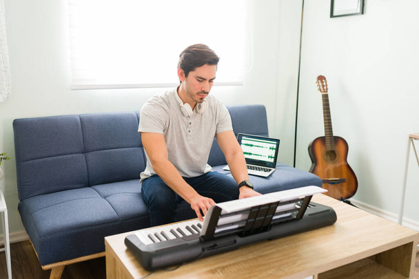 Привлекательный мужчина-музыкант, играющий на пианино, сидя в гостиной. Творческий композитор записывает новую песню дома - Фото, изображение