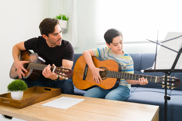 Insegnante di musica appassionata che suona la chitarra acustica insieme a uno studente di ragazzo che impara gli accordi di chitarra di una bella canzone - Foto, immagini