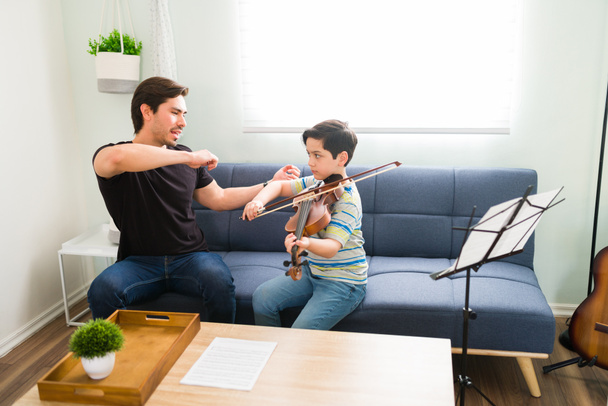 Megtanítom, hogyan kell helyesen hegedülni. Jóképű zenetanár privát hegedűleckéket ad egy kaukázusi elemi fiúnak otthon. - Fotó, kép