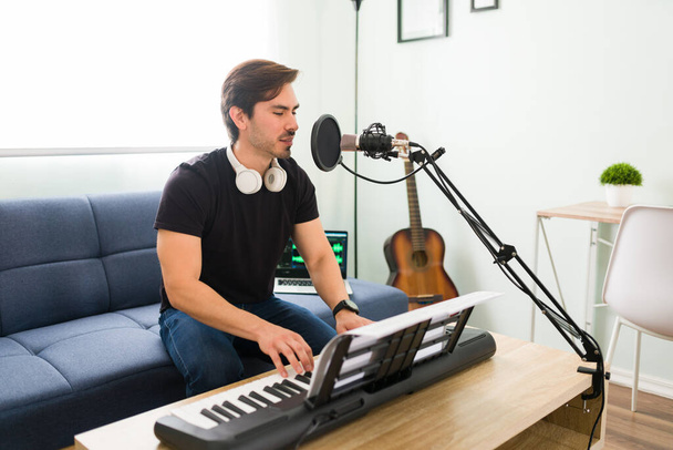 Singing my new song. Handsome young musician and composer recording a song with a microphone at home while playing the piano  - Фото, зображення