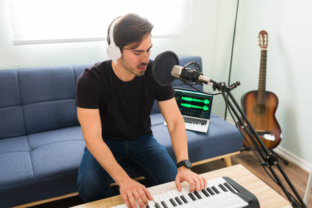 Vonzó férfi énekes és zenész fülhallgatóval zongorázni, miközben rögzíti az új dalt otthon - Fotó, kép