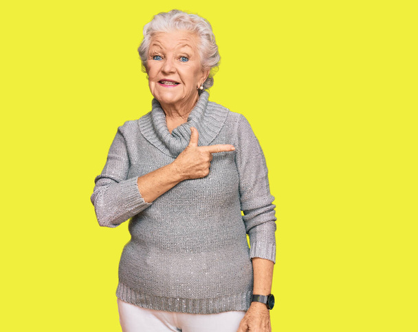 Senior grijsharige vrouw draagt casual winter trui vrolijk met een glimlach op het gezicht wijzend met hand en vinger naar de zijkant met vrolijke en natuurlijke expressie  - Foto, afbeelding