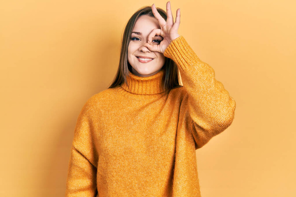 Young hispanic girl wearing casual clothes doing ok gesture with hand smiling, eye looking through fingers with happy face.  - Photo, Image