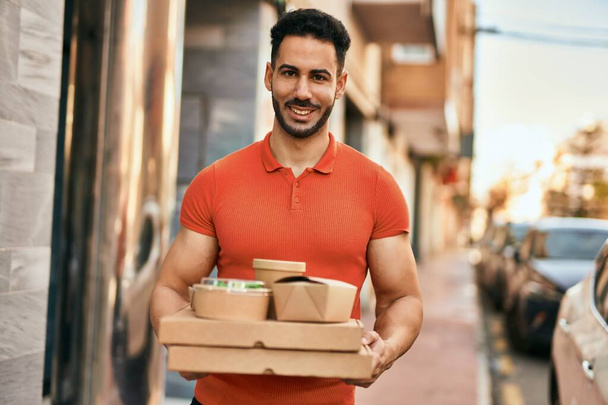 De jonge Spaanse man glimlacht gelukkig terwijl hij eten meeneemt naar de stad.. - Foto, afbeelding
