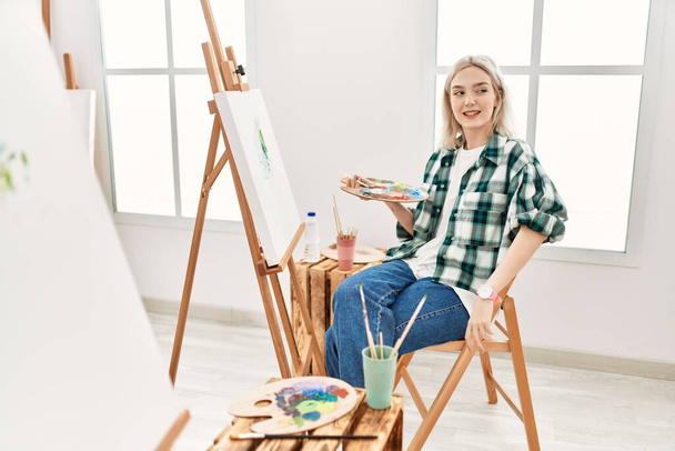 Sanat stüdyosunda resim yapan genç sanatçı kadın yüzünde gülümsemeyle, doğal ifadeyle yan yana bakıyor. Kendinden emin gülen.  - Fotoğraf, Görsel