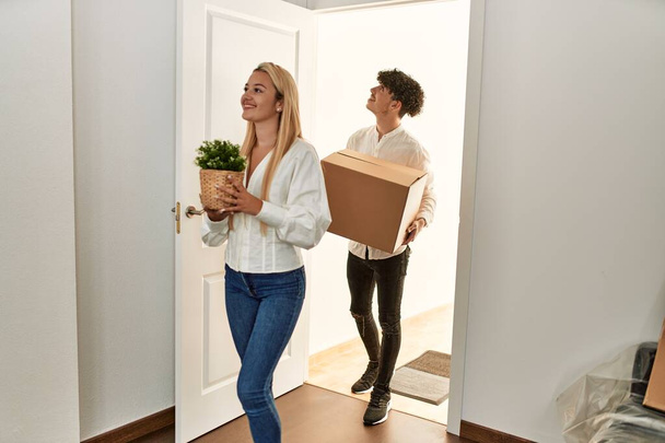Молода красива пара посміхається щасливий тримає картонну коробку входу в новий будинок
. - Фото, зображення
