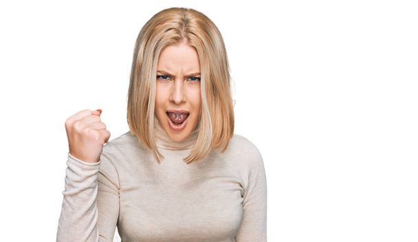 Young blonde woman wearing casual clothes angry and mad raising fist frustrated and furious while shouting with anger. rage and aggressive concept.  - Foto, Imagen