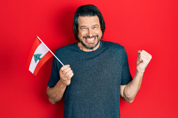 Середньовіччя кавказький чоловік тримає прапор Лівану кричав гордо, святкуючи перемогу і успіх дуже схвильований піднятою рукою
  - Фото, зображення