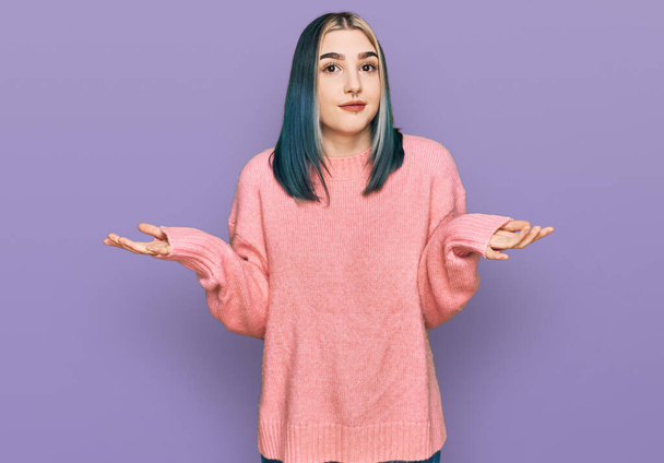 ピンクのウールの冬のセーターを身に着けている若い現代の少女は、腕や手を上げて混乱した表情。疑わしい概念.  - 写真・画像