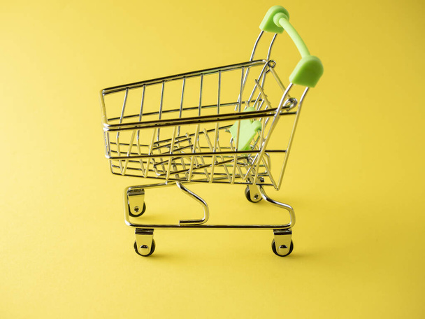 Κοντινό πλάνο πράσινων καροτσιών σε κίτρινο φόντο. Σχέδιο πωλήσεων. Καλάθι, προϊόντα. Πλευρική άποψη - Φωτογραφία, εικόνα