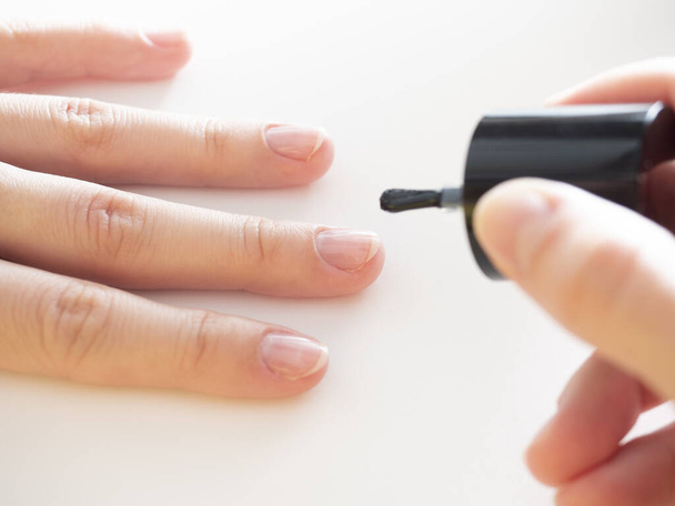 aanbrengen van een kleurloze basis op de nagel. Manicure thuis, nagelverzorging. - Foto, afbeelding